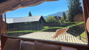 A room with a view of a wooden deck, a lounge chair, and a building in the background.