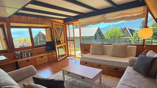 A spacious living area with a large window, wooden furniture, and a view of mountains.