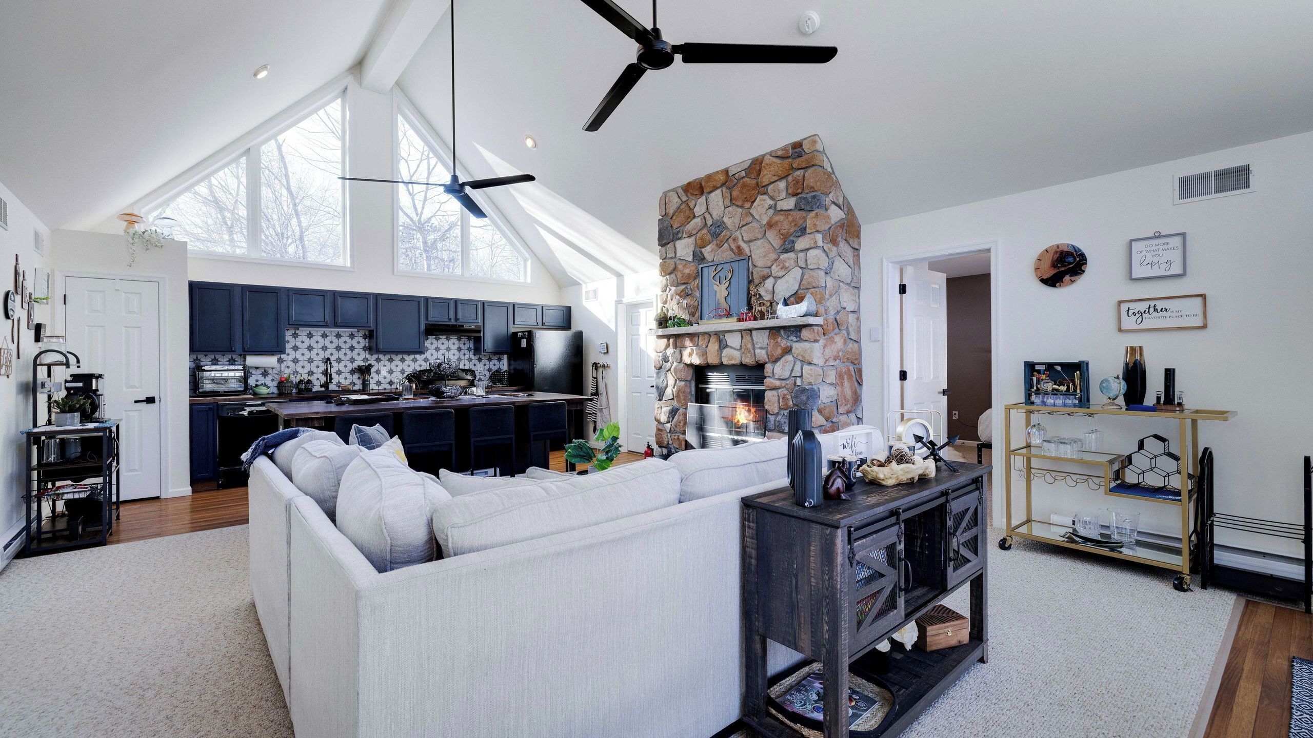 Una sala de estar moderna con chimenea de piedra, un sofá grande y una cocina al fondo.