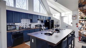 A modern kitchen with dark blue cabinets, a central island, and a stone accent wall. - Peak & Pine by Avantstay Hot Tub + Fire Pit Mins to Ski + Lake Harmony (Albrightsville)