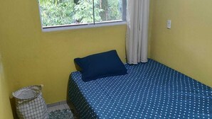 A small room with a single bed, a window with curtains, a small trash bin, and a green rug. - Pousada beira rio  (Rodeio)