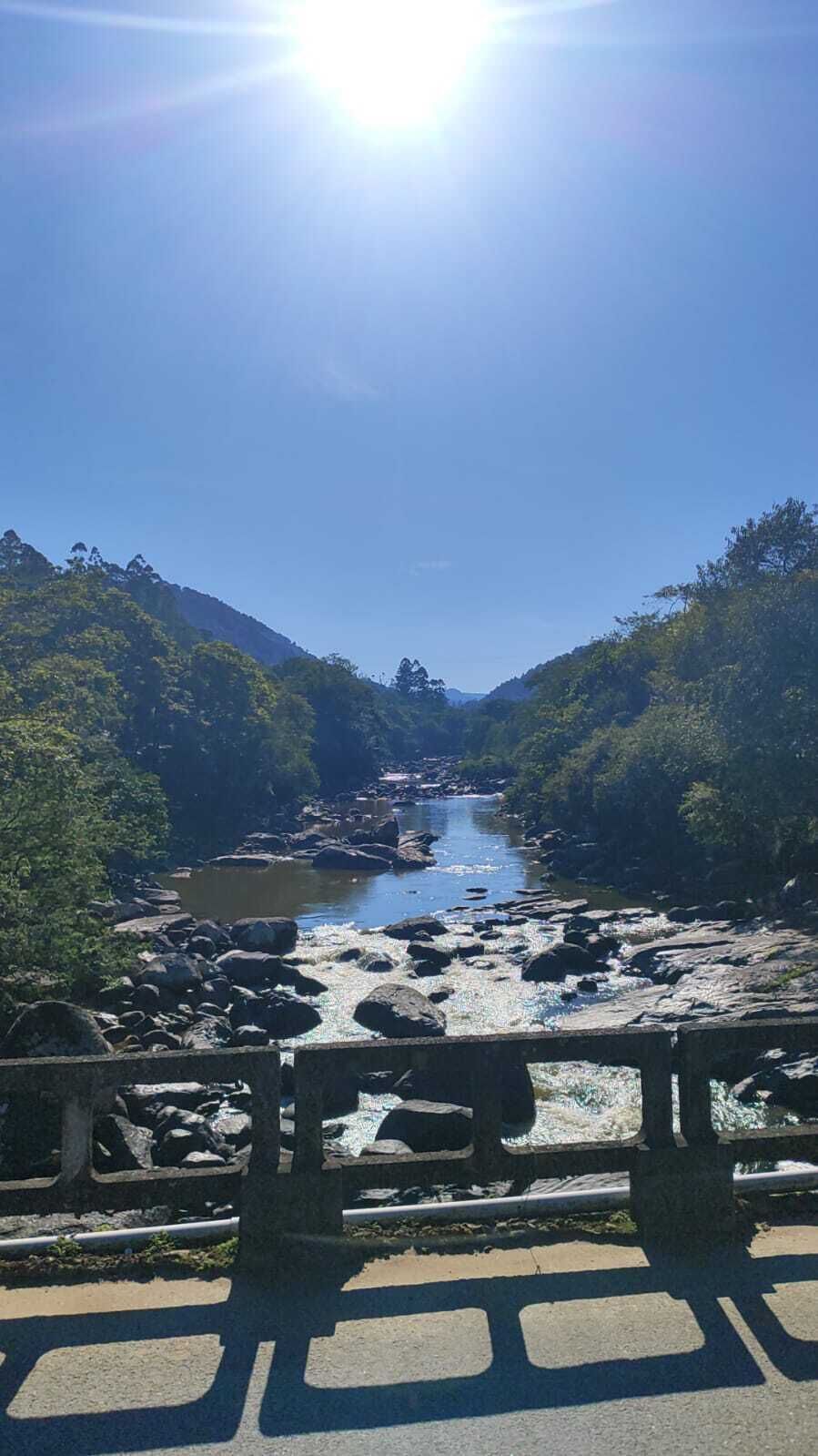 Um rio com pedras e árvores, uma ponte de madeira e um céu limpo.