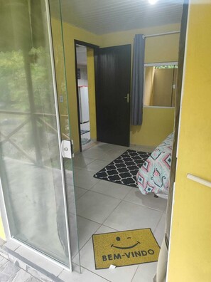 A room with a glass door, a bed with patterned bedding, a black and white rug, and a welcome mat with a smiley face. - Pousada beira rio (Rodeio)