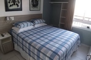Un dormitorio con cama, mesita de noche, armario y ventana con cortinas.