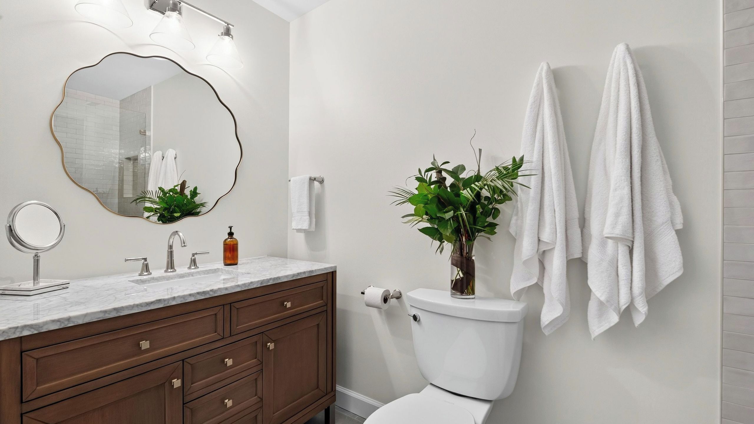 Ein Badezimmer mit Marmorwaschtisch, einem runden Spiegel, einer Toilette und zwei Handtüchern, die an der Wand hängen.