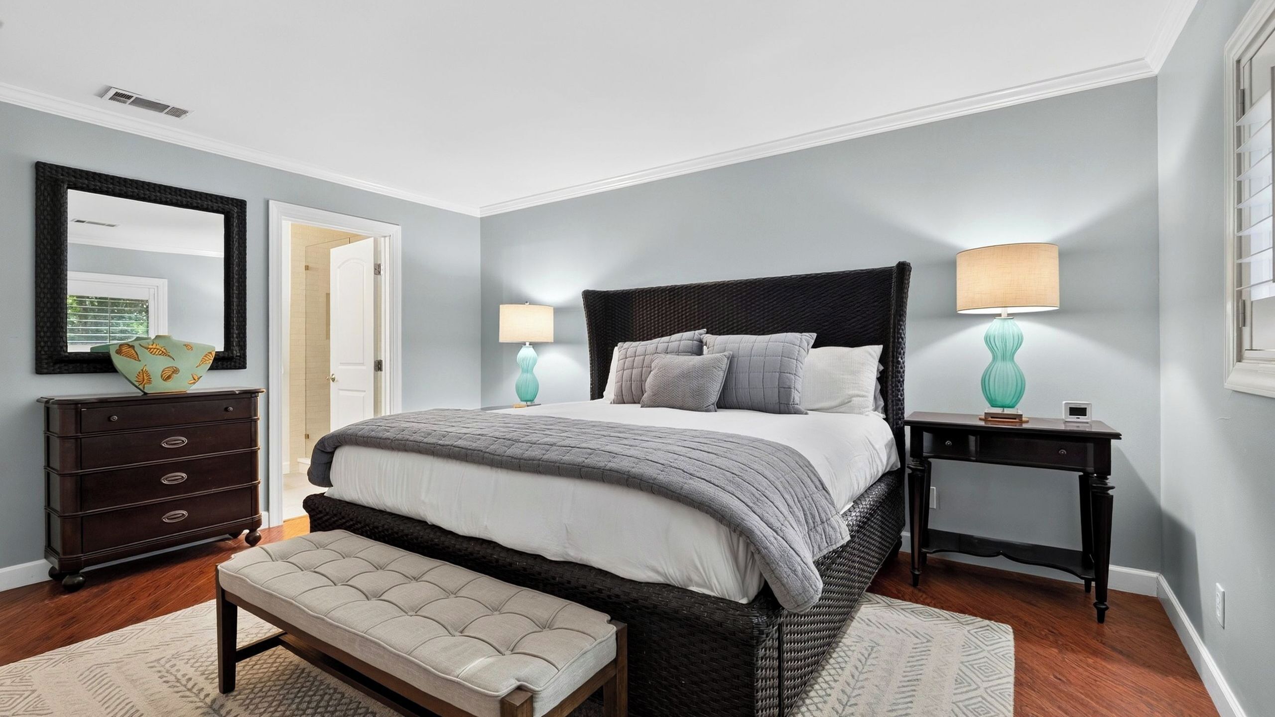 A bedroom with a bed, bedside tables, a dresser, a bench, and a mirror.