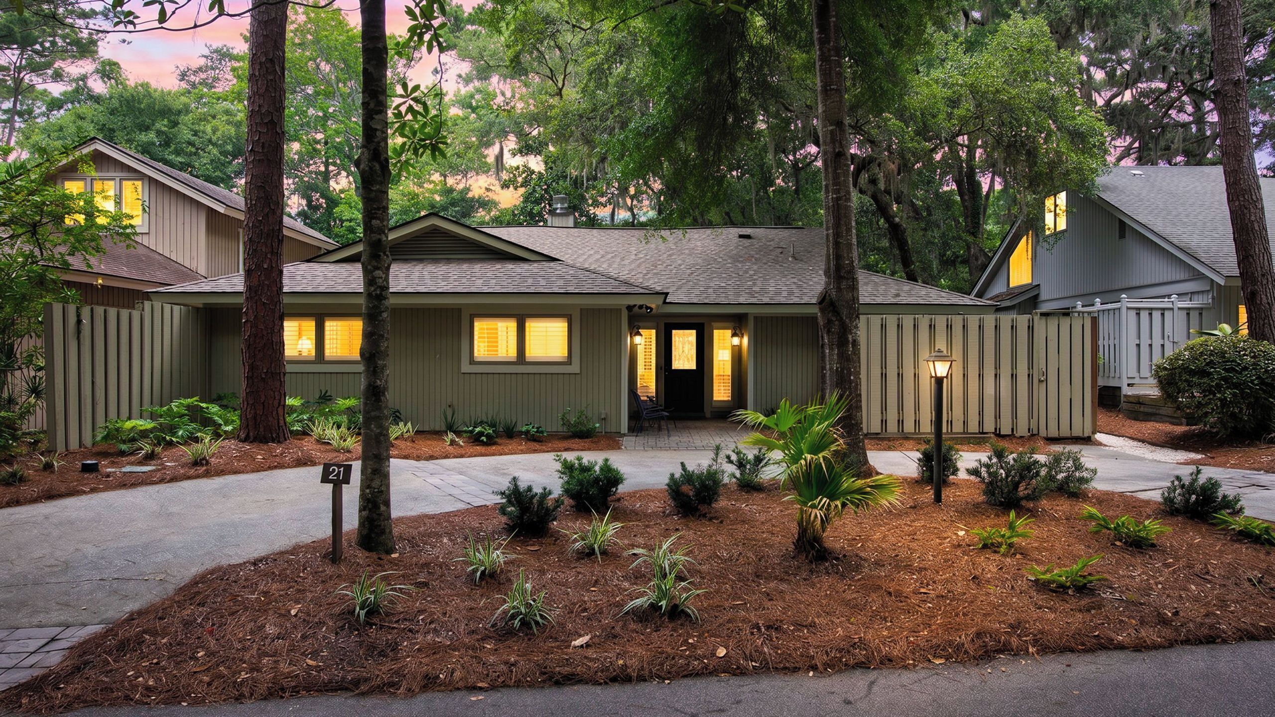 A two-story house with a front porch, a driveway, and a well-maintained garden with small plants and mulch.