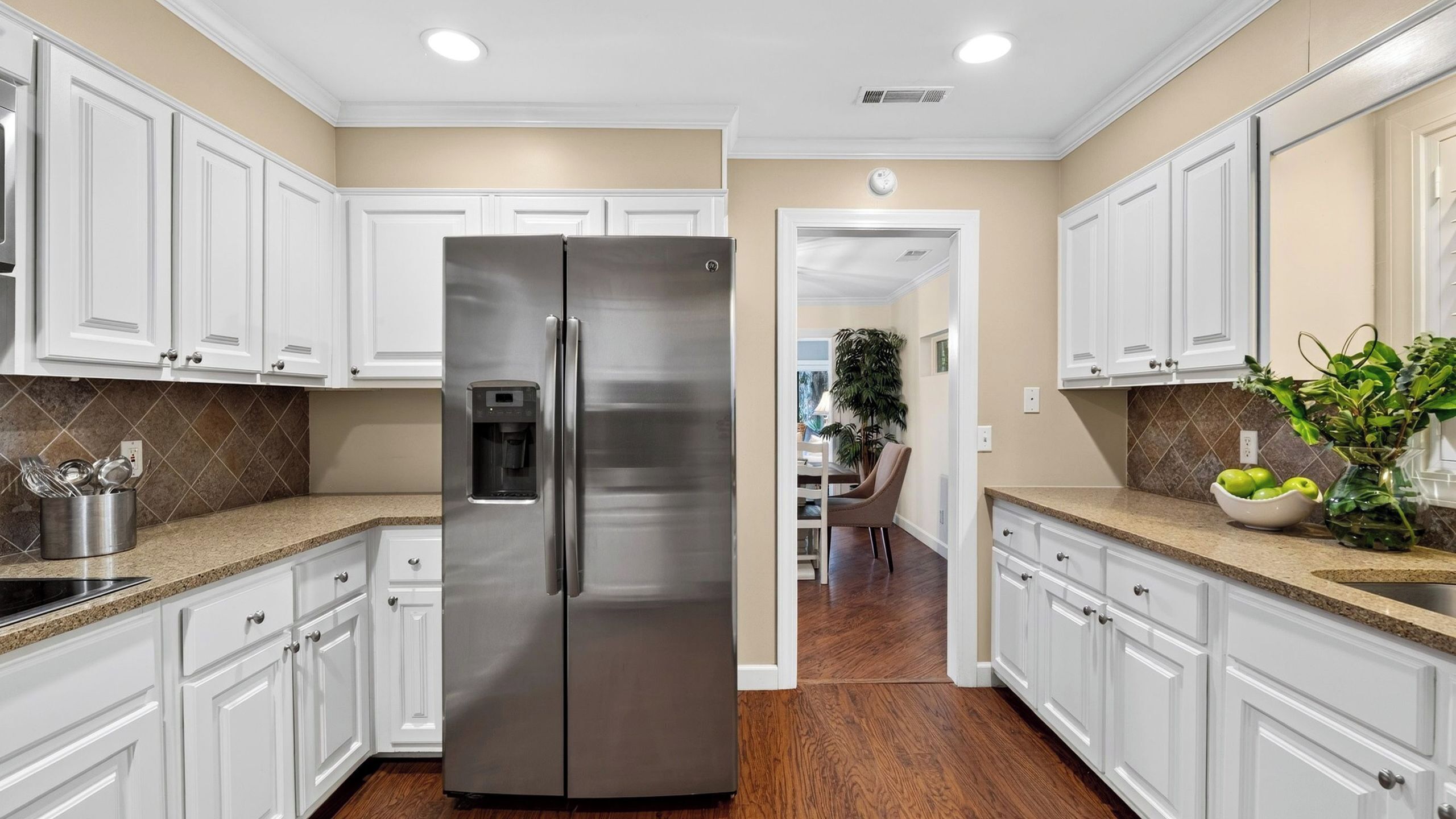 A kitchen with white cabinets, a stainless steel refrigerator, granite countertops, and a wooden floor.
