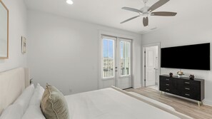 A bedroom with a bed, a dresser, a ceiling fan, a TV, and a door leading to a balcony. - High Tide by Avantstay Luxe Beach Retreat Shared Pool + Hot Tub Walk to Beach (Panama City Beach)