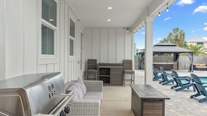 Eine überdachte Terrasse mit Grill, Korbmöbeln und Sitzgelegenheiten im Freien.