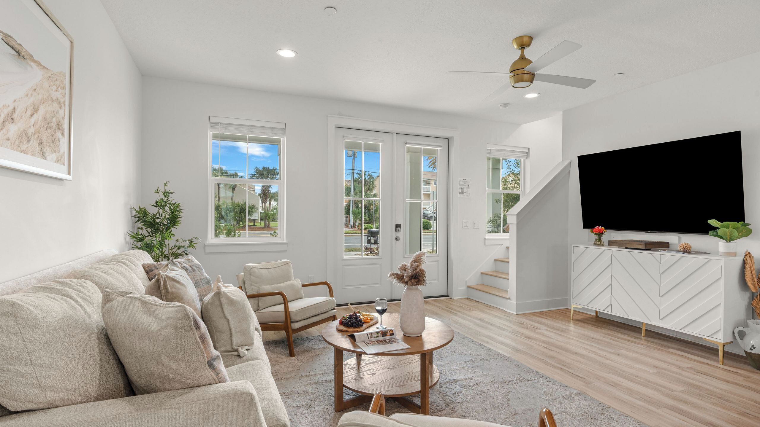 A modern living room with a sofa, chairs, a coffee table, a TV, and a staircase leading to an outdoor area.