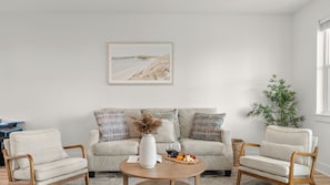 Ein Wohnzimmer mit einer Couch, zwei Sesseln, einem Couchtisch, einem gerahmten Bild und einer Topfpflanze.