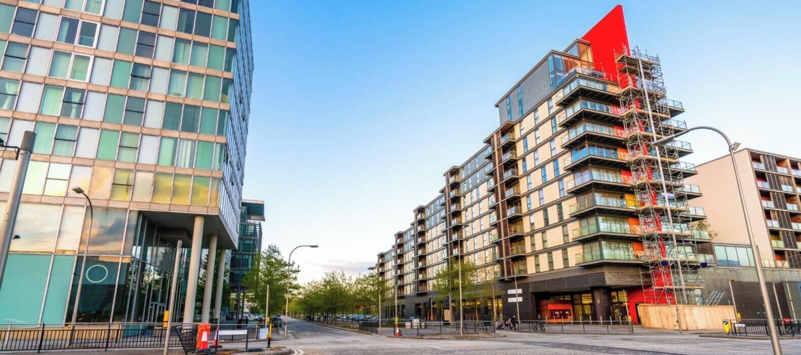 Une rue moderne, située en milieu urbain, bordée d’immeubles de grande hauteur, dont l’un se distingue par son sommet rouge.