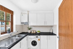 A compact kitchen with a washing machine, a sink, and a window with a view of greenery. - Detached 4BR House in Monkston Park • Driveway Parking • Fast WiFi • Smart TVs • Yoko Property (Milton Keynes)