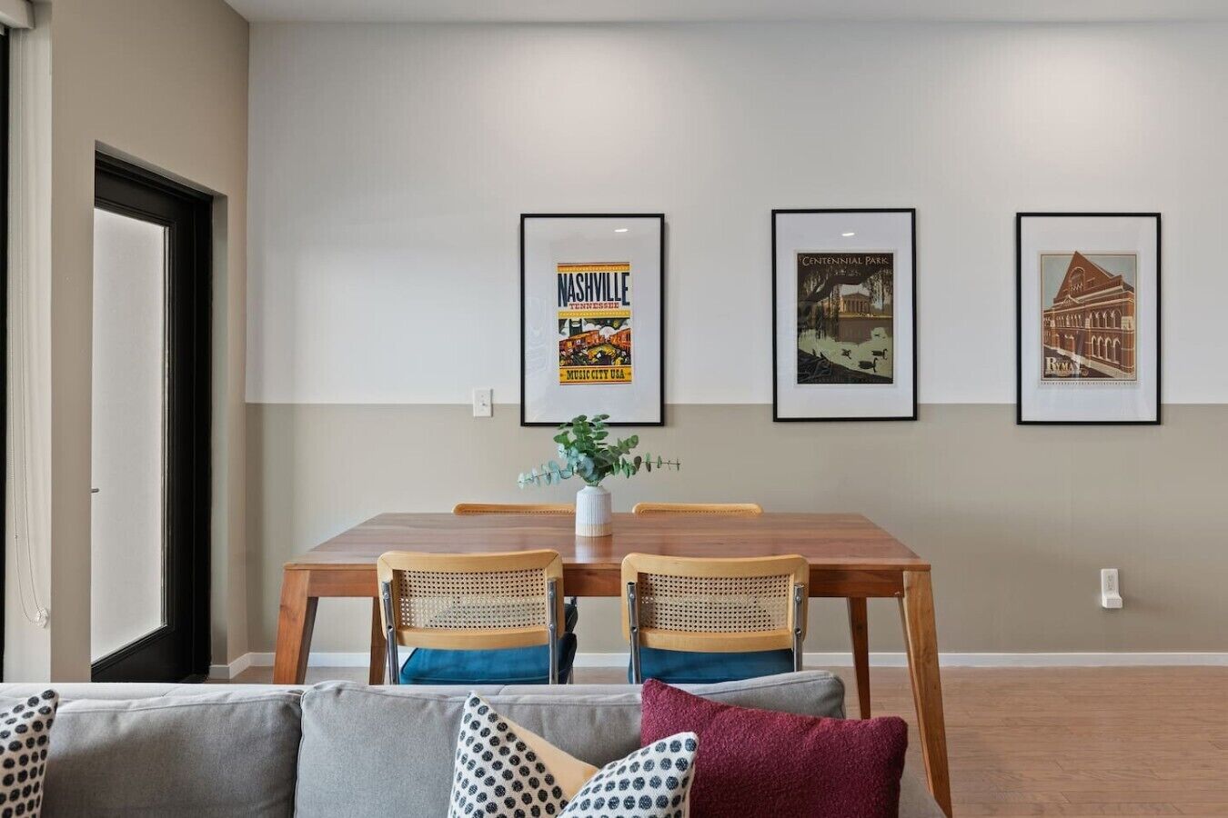 A dining area with a wooden table and chairs, framed pictures on the wall, and a plant on the table.