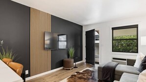 A modern living room with a flat-screen TV, a sofa, a coffee table, and a large window with a view. - Walk to Music Row and Vanderbilt, Only 1 Mile to Broadway (Nashville)