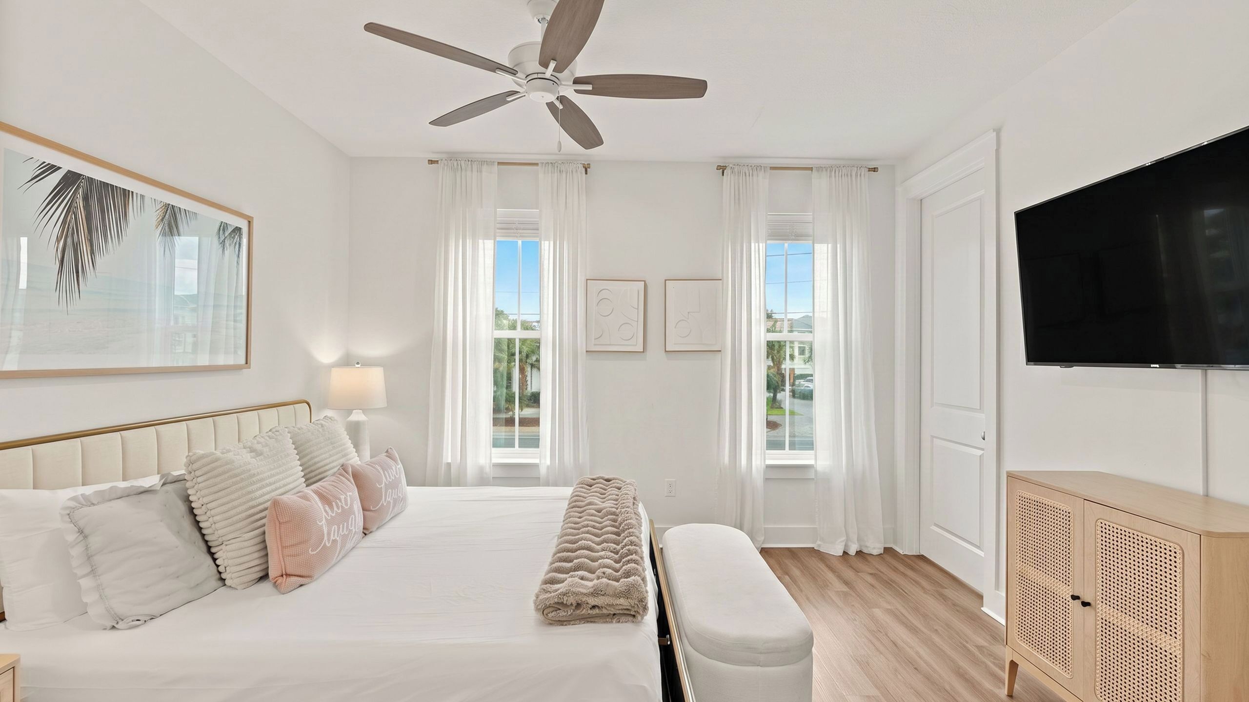 A bedroom with a bed, a ceiling fan, a TV, and a window with curtains.