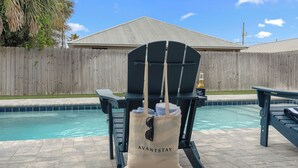 A poolside chair with a bag labeled 'AVANTSTAY' and a bottle of 'Good Times' beer. - Low Tide by Avantstay Walk to Beach Shared Pool + Hot Tub Near St. Andrews (Panama City Beach)