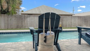 A poolside chair with a bag labeled 'AVANTSTAY' and a bottle of 'Good Times' beer. - Low Tide by Avantstay Walk to Beach Shared Pool + Hot Tub Near St. Andrews (Panama City Beach)