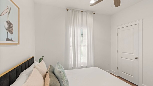 A bedroom with a bed, a ceiling fan, a door, and a window with curtains. - Low Tide by Avantstay Walk to Beach Shared Pool + Hot Tub Near St. Andrews (Panama City Beach)