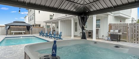 A backyard with a hot tub, a pool, and a covered patio area.