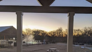 A covered outdoor area with a table and chairs, a fire pit, and a view of a fenced field. - Pet-Friendly Cabin w/ Loft | Pool, Fire Pit & River (Hutto)