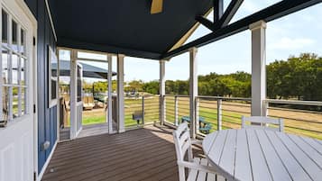 A covered outdoor area with a wooden deck, white furniture, and a view of a park with playground equipment.