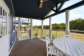 A covered outdoor area with a wooden deck, white furniture, and a view of a park with playground equipment.