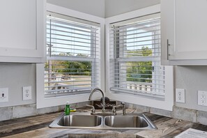 A kitchen with a double sink, two windows with blinds, and a welcome sign.