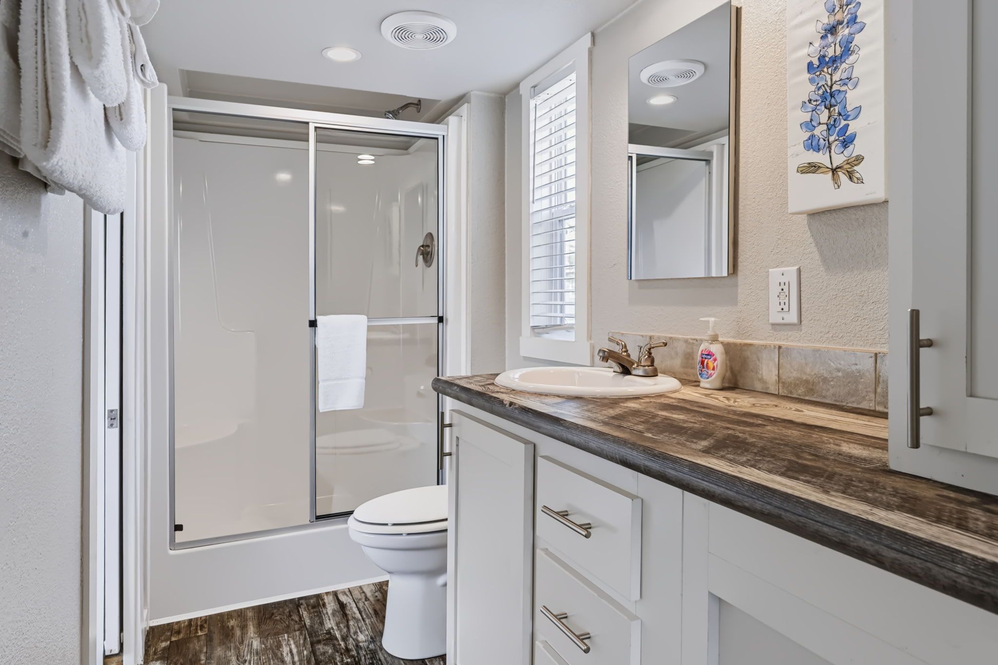 A modern bathroom with a glass shower enclosure, a toilet, and a vanity with a wooden countertop.