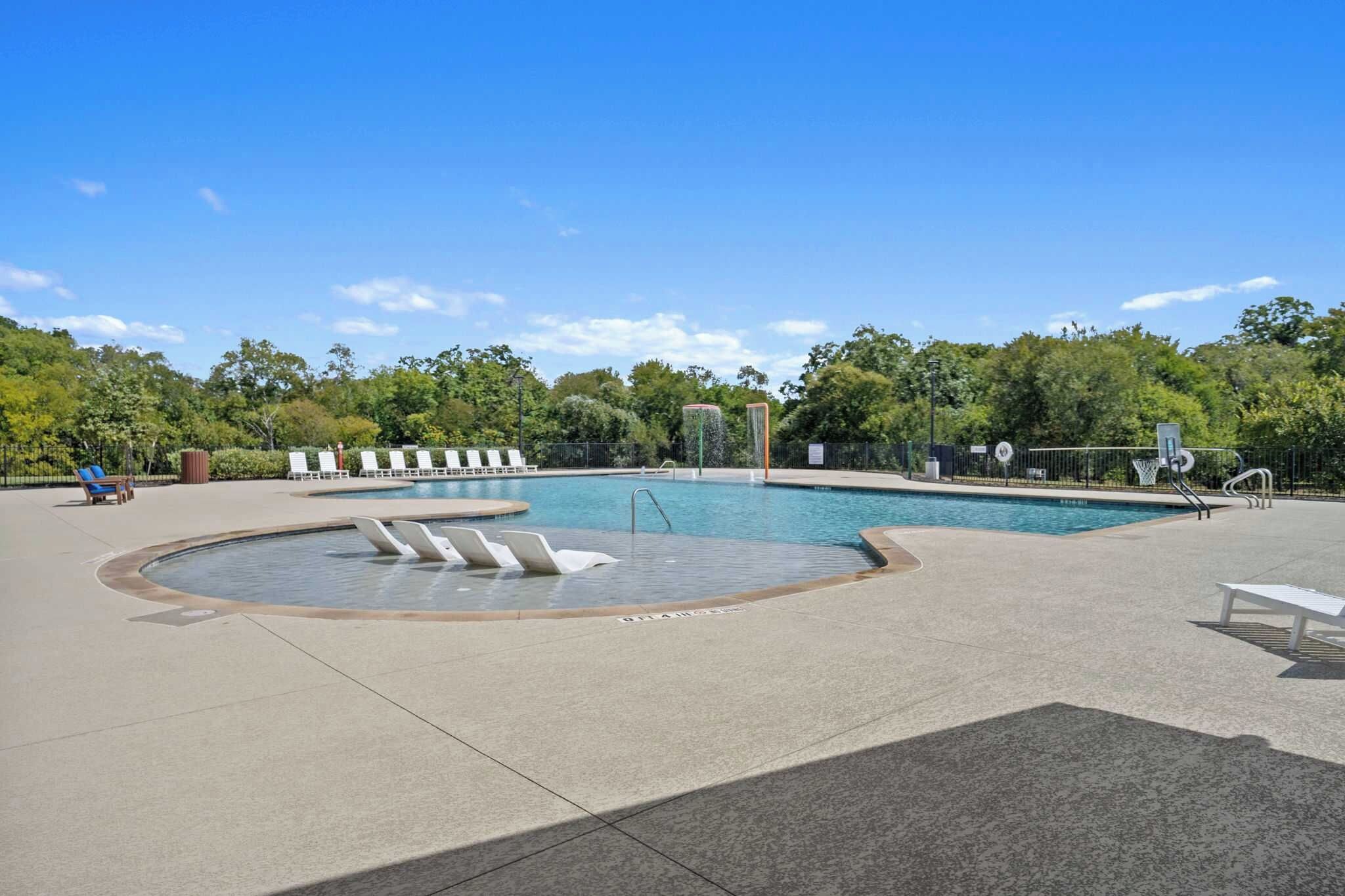 Una piscina con hidromasaje circular, sillas de descanso y aro de baloncesto.