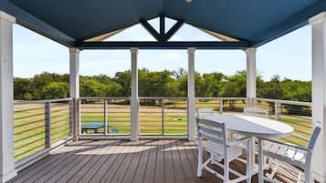 Un'area esterna riparata con un pavimento in legno, un tavolo con sedie e vista su un campo verde.