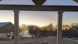 A covered outdoor area with a table and chairs, a fire pit, and a view of a fenced field.