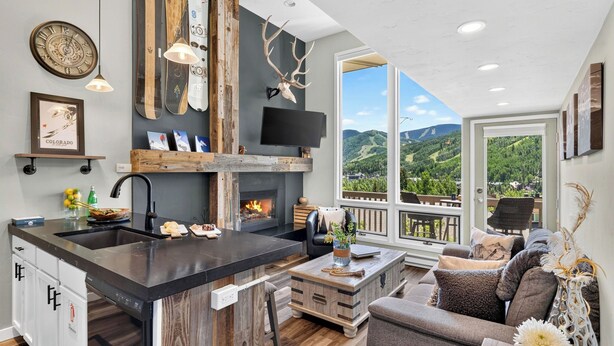 A modern kitchen with a fireplace, a large window with a mountain view, and a cozy seating area. - Serenity by the Slopes Steps to Trails + Free Bus to Slopes Balcony + Views (Vail)