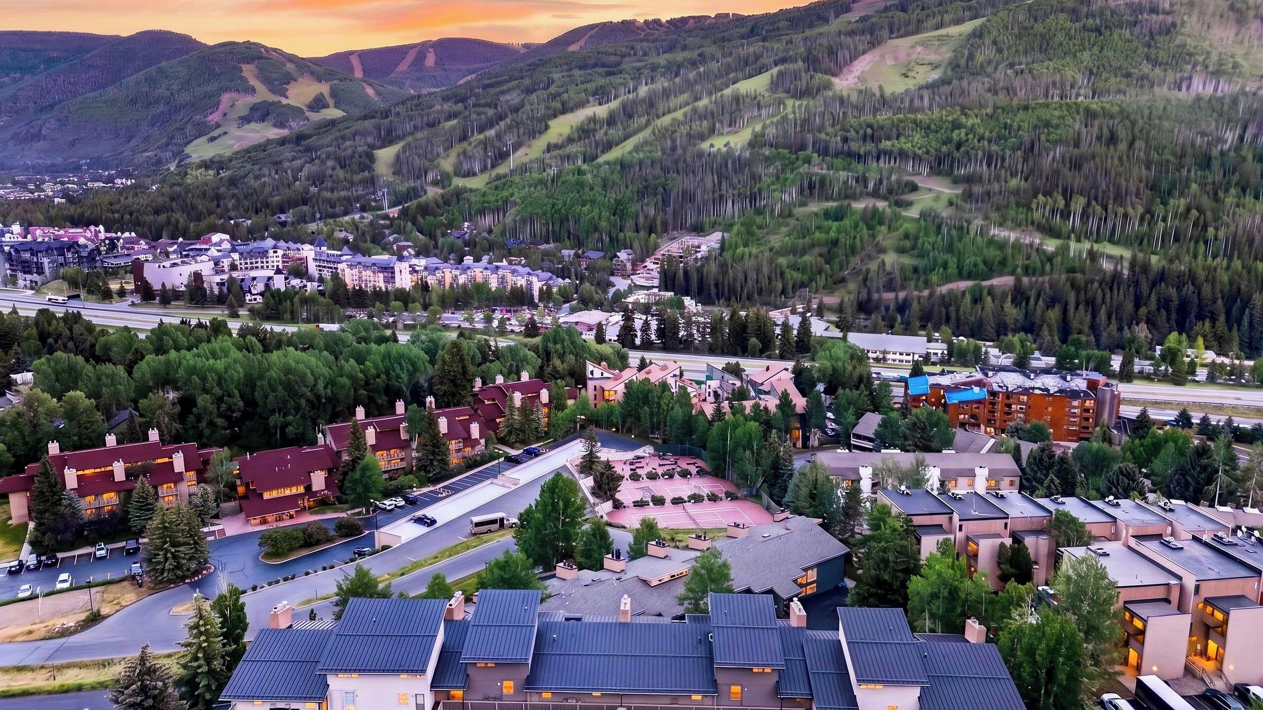 A town with a mix of residential and commercial buildings, a parking lot, and a mountainous backdrop.