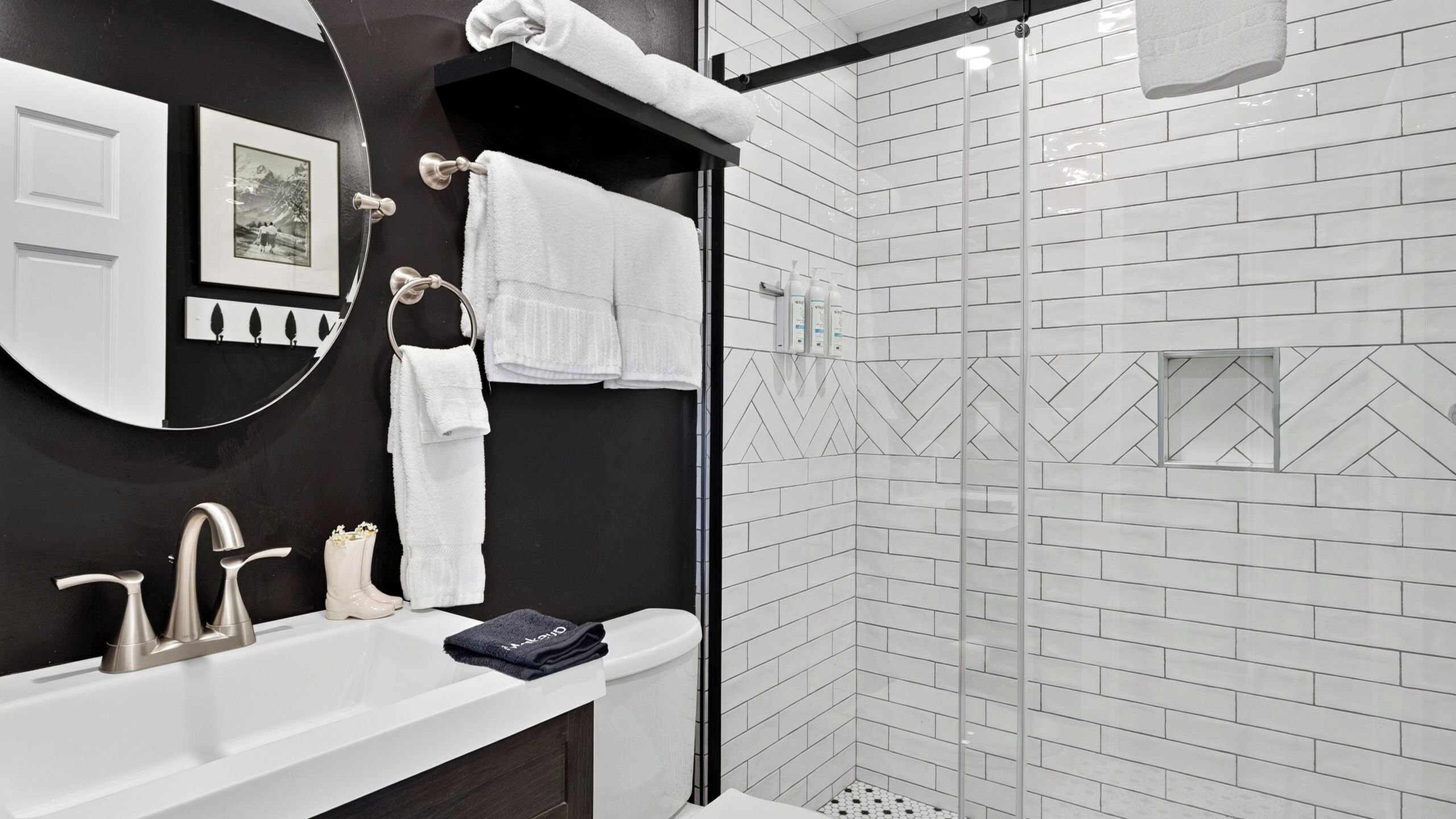 A modern bathroom with a white sink, dark vanity, and a glass-enclosed shower.
