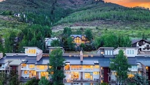 A multi-story residential building with a prominent central structure, surrounded by other houses, set against a mountainous backdrop. - Serenity by the Slopes Steps to Trails + Free Bus to Slopes Balcony + Views (Vail)