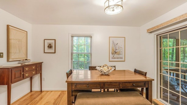 A dining area with a wooden table, bench, and chairs, a window with blinds, and artwork on the walls. - Total Escape LKA home w/ gameroom and water access (Mineral)