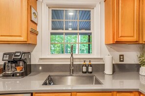 A kitchen with a window, a coffee maker, two bottles, and a roll of paper towels.