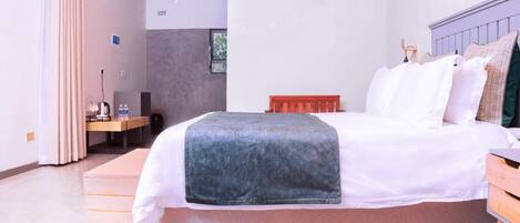 A bedroom with a bed, a wooden bench, a desk with a chair, and a window.
