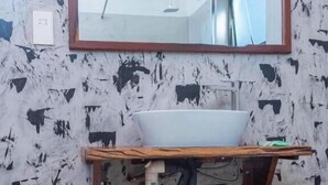 A bathroom with a white sink on a wooden vanity, a mirror above it, and a wall with a textured pattern. - The Woodlands Retreat (Chinhoyi)