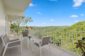 A balcony with white chairs and a glass table, overlooking a lush green landscape. - Casa Brisa w/ Heated Pool + Mt. View + River (Las Marías)