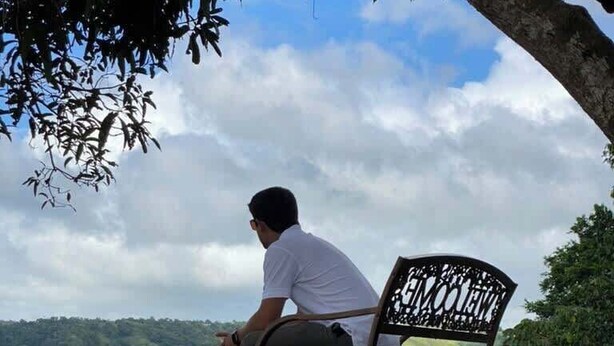 Un homme est assis sur un banc, face à un paysage vallonné.