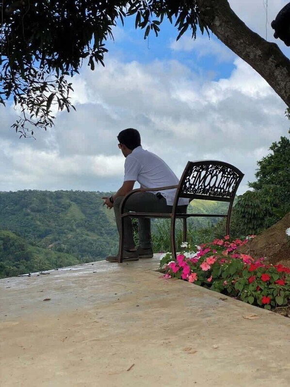 A man sitting on a bench with a view of a hilly landscape.