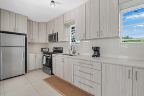 A modern kitchen with stainless steel appliances, light wood cabinets, and a large window with a view.