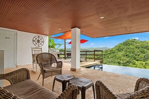 A covered outdoor area with wicker furniture, a pool, and a view of a forested landscape.