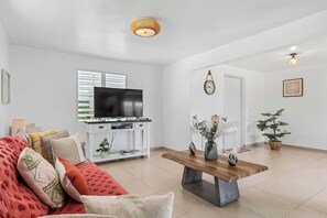 Una sala de estar con televisor de pantalla plana, una mesa de centro de madera, un sofá con cojines estampados y una planta en maceta.