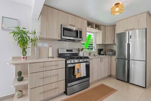 A modern kitchen with a stainless steel refrigerator, a microwave, a stove, and a sink. There are wooden cabinets and a countertop. - Casa Verde at Hacienda Serena w/ Mt. View + River (Las Marías)