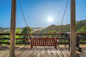 Un banco de madera para columpios con vista a un paisaje exuberante y una parrilla de barbacoa.