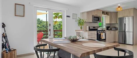 A modern kitchen with a central island, a dining area with chairs, and a view through a glass door.